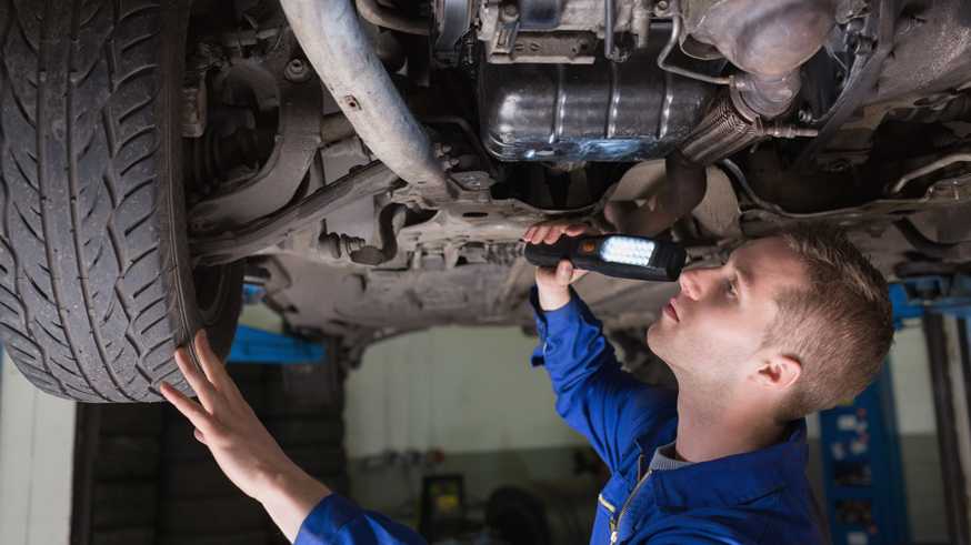 Male mechanic examining car using flashlight